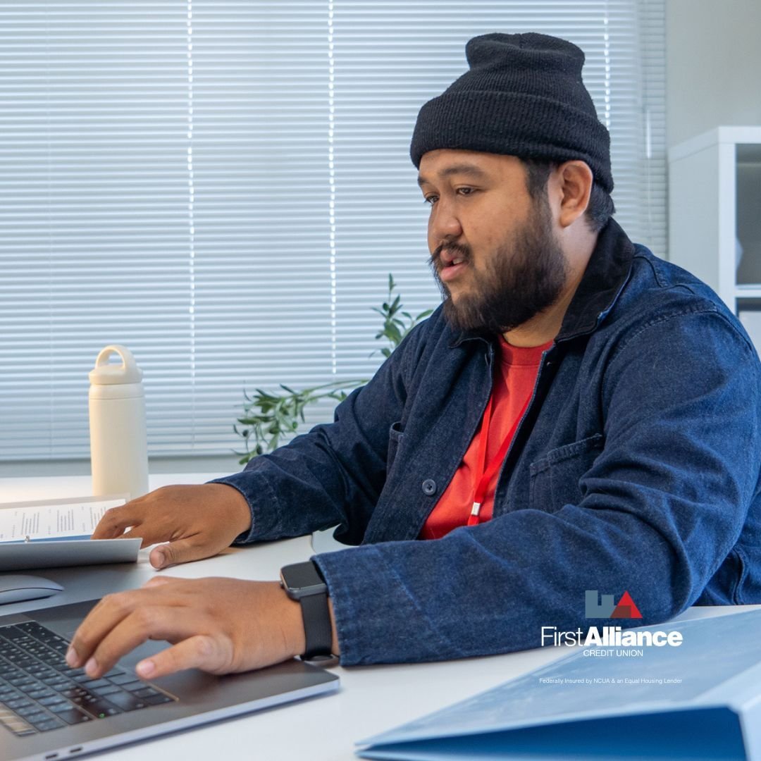 man with a beanie on his head working on his computer reviewing the My Money tool at First Alliance