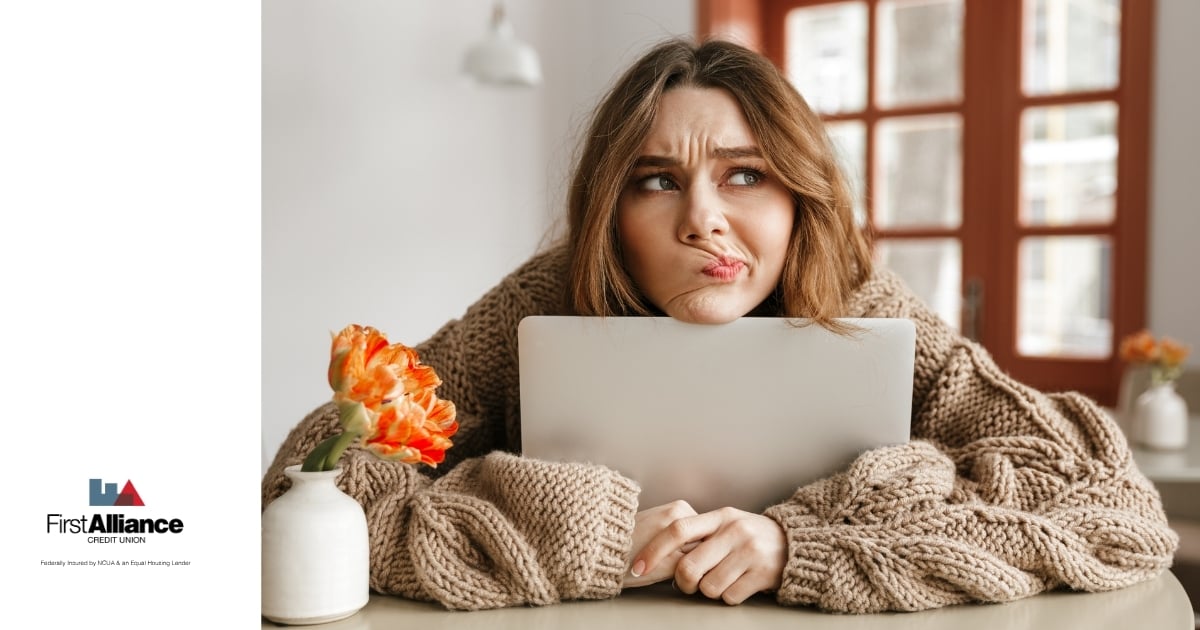 woman in sweater with head on laptop reviewing finances