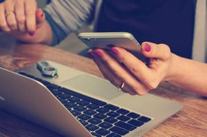 Close up of woman holding an iphone in one hand and a laptop on our desk, using online banking to help make switching banks easier | First Alliance Credit Union 