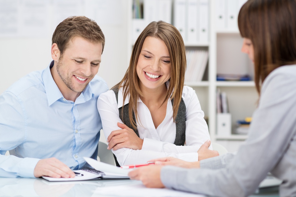 Investment adviser giving a presentation to a friendly smiling young couple seated at her desk in the office.jpeg