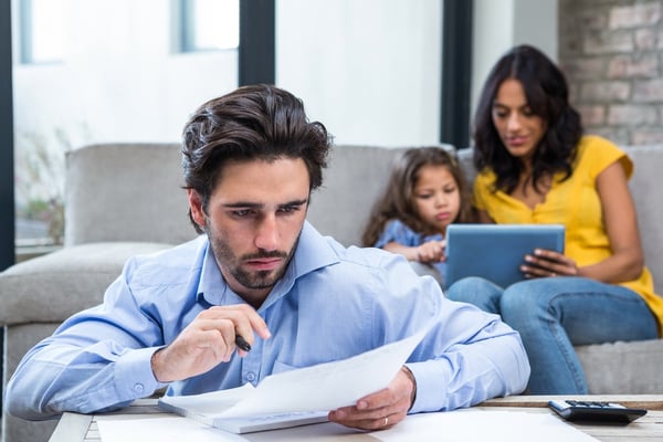 Thoughtful father refinancing a loan in living room while wife and daughter are on the sofa first alliance credit union