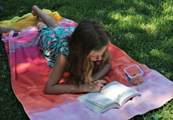 Girl on a blanket outdoors, reading a book