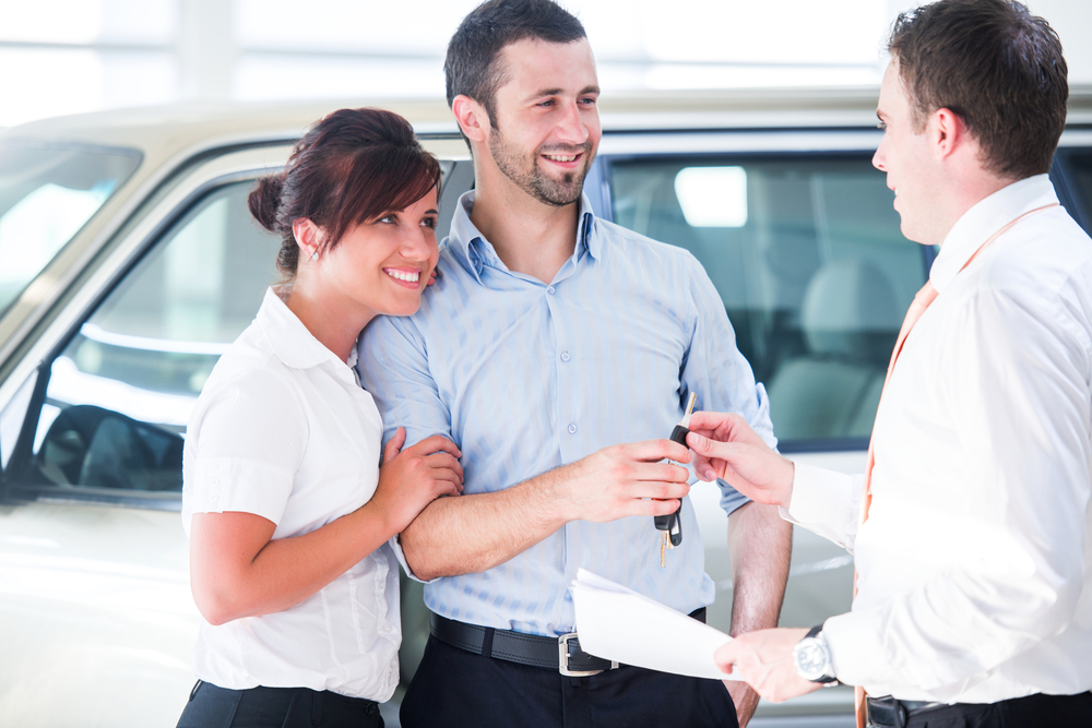 Smiling couple buying a new car from a salesman