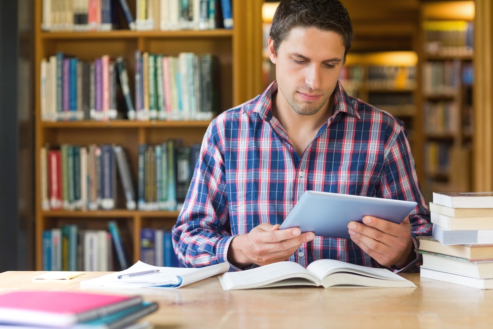 Concentrated mature male student using tablet PC at desk in the library