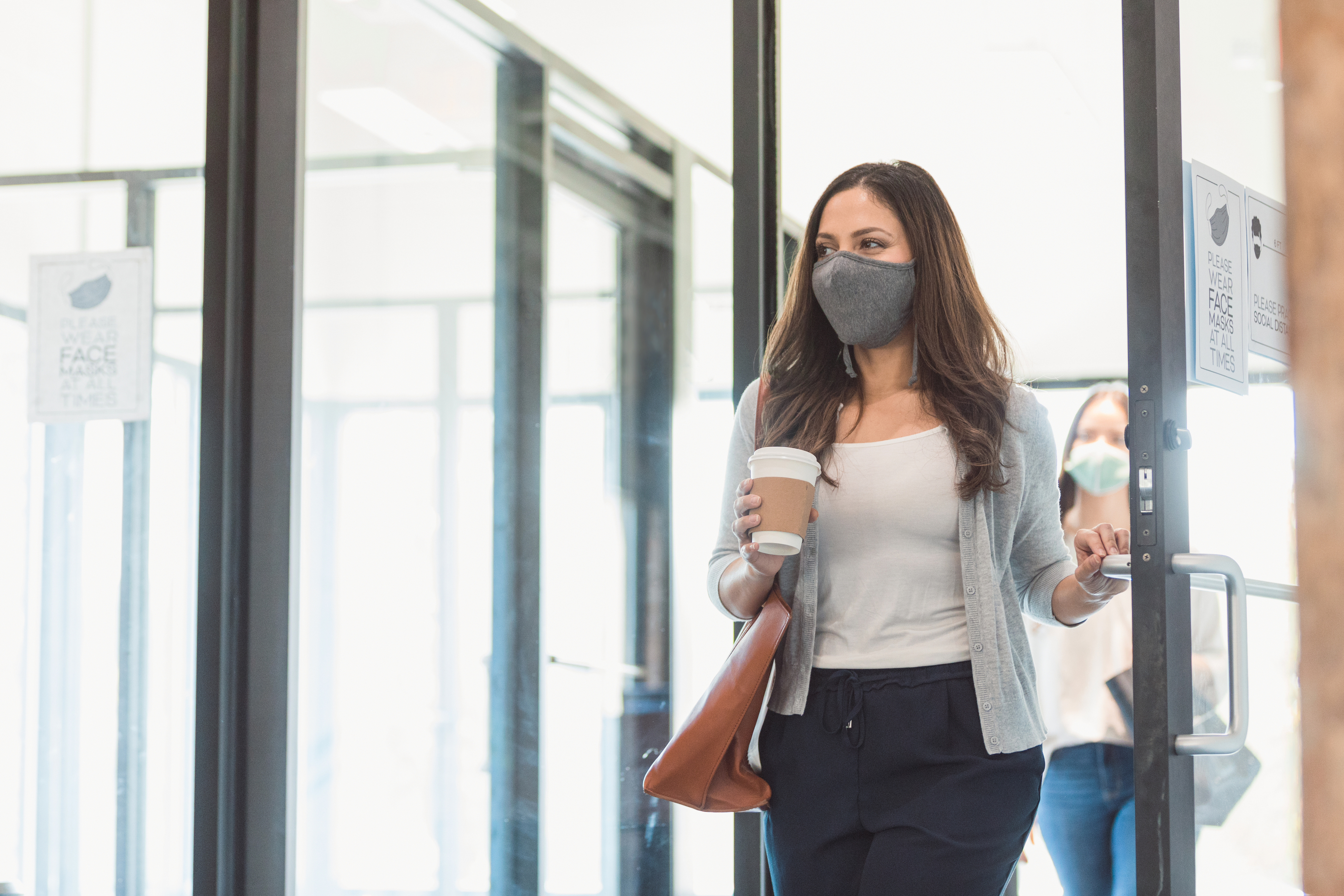 Woman wearing a mask and carrying a cup of coffee walking through an office | First Alliance Credit Union